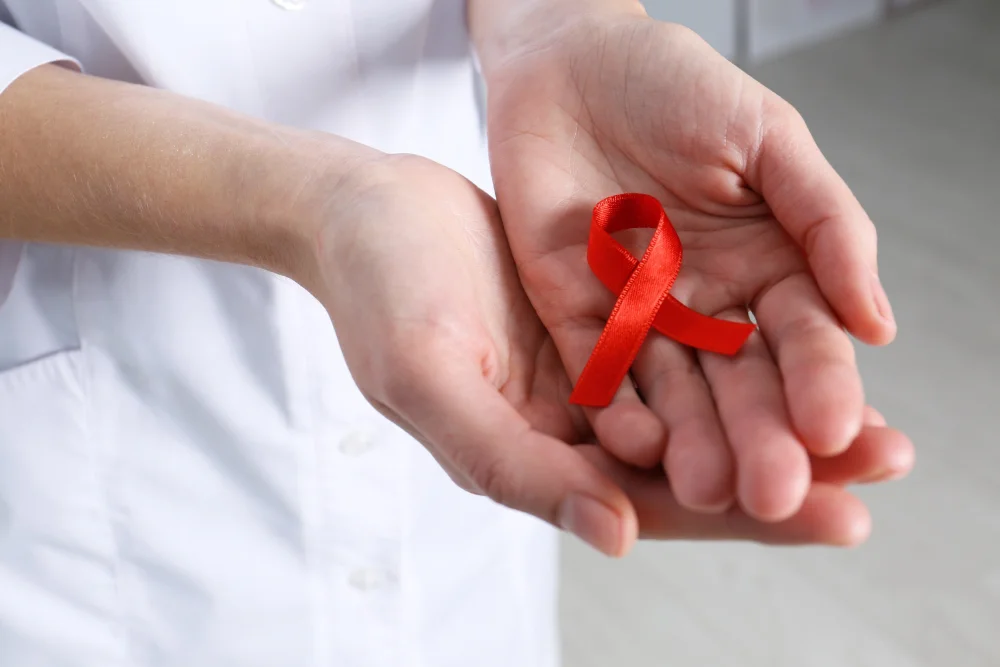 Person holding red AIDS awareness ribbon.