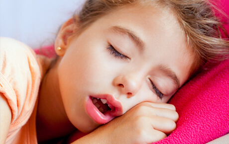 Young girl sleeping peacefully on pink pillow.